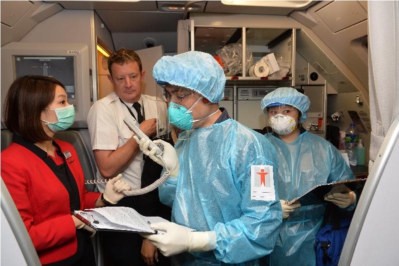 配戴个人防护装备的卫生署港口卫生处人员于航班抵港后，在机长协助下登机调查。